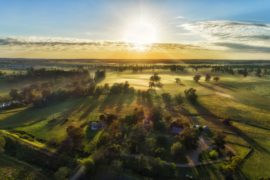 Secluded farm homestead on agriculture cultivated fields near Macquarie river in Dubbo town of Australia - aerial sunrise view.